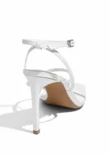 Sandalias de tacón alto color blanco, con punta cuadrada, tira delgada sobre los dedos, tira fina alrededor del tobillo con hebilla metálica y tacón fino.