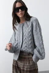 Cardigan de tejido de punto color marrón chocolate, con diseño de trenzas en el frente y mangas. Presenta cuello redondo, cierre frontal con botones al tono y puños acanalados.