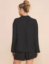 Blusa Allie Rose de color negro, corte holgado con escote en V cruzado y cuello camisero. Presenta mangas largas amplias con puños sutilmente fruncidos y diseño de silueta fluida.