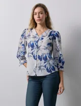 Blusa de gasa estampada con flores azules y blancas, marca Sioni. Tiene escote en V, abertura frontal con botones y mangas 3/4 con puños fruncidos y botón.