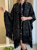 Ruana de tejido de punto color negro con sutil hilo brillante integrado y flecos largos en los bordes.