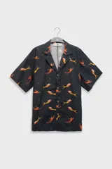 Camisa de manga corta con cuello camp-collar, frente abotonado con botones de coco y corte relajado. Presenta un estampado integral de sirenas sobre fondo negro.