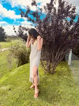 Vestido largo de lino color beige con cuello redondo, sin mangas, abertura lateral y terminación con flecos. Presenta detalle de cuero en el escote.