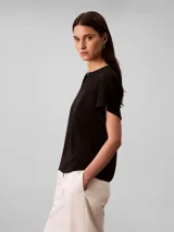 Blusa Calvin Klein de manga corta en color negro, confeccionada en tejido fluido de crêpe de chine. Cuenta con un diseño de cuello redondo con escote en V y una barra metálica decorativa en el centro del cuello.