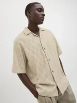 Camisa de manga corta Jack & Jones con cuello resort y cierre de botones. Diseño con estampado de espiga en tonos beige y blanco. Confeccionada en tejido dobby 100% algodón.