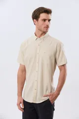 Camisa de manga corta confeccionada en mezcla de lino y algodón, color beige, con cuello camisero abotonado, bolsillo frontal en el pecho y cierre de botones.