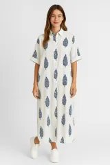 Vestido camisero largo color blanco con estampado de hojas azules, de corte holgado, manga corta y cuello camisero.
