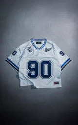 Camiseta estilo jersey de fútbol americano en color blanco con detalles en azul. Presenta el número 90 estampado en el frente y en las mangas, con el logo de la marca Luxo y la inscripción Ravers en el pecho.