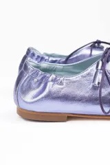 Zapato tipo blucher de piel metalizada en color violeta, con diseño híbrido entre blucher y bailarina. Presenta cierre con cordones y borlas decorativas, acabado sin ribete con ondas laterales y elástico en la parte trasera para un ajuste óptimo. Interior y suela de cuero.