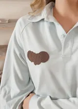 Buzo celeste de manga larga con cuello polo y cierre frontal de botones. Presenta un parche marrón bordado en el pecho.