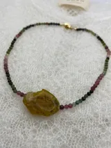 Collar de cuentas pequeñas facetadas de piedras naturales en tonos verdes, rosados y negros, con un dije central de piedra irregular en tono ocre.