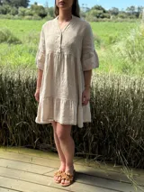 Vestido corto de lino color beige claro, con cuello mao, escote con botones de nácar, mangas tres cuartos con volados y ruedo con volado.