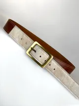 Cinturón de cuero marrón con detalle de pelo natural en tono claro en la parte frontal y hebilla metálica rectangular en color bronce.