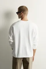 Camiseta relaxed fit de manga larga color blanco, confeccionada en tejido de modal y algodón fluido, con cuello redondo y puños de rib.