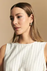 Top sin mangas color beige con finas rayas verticales negras. Presenta un diseño con lazada ajustable en el lateral de la cintura.