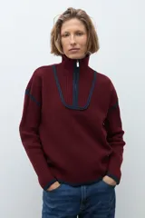 Sweater de punto color crudo con cuello alto y cierre frontal parcial. Presenta detalles de vivos en color marrón en el cuello, hombros y ruedo, con diseño de manga larga.
