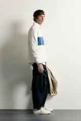 Remera polo de manga larga de corte regular fit, confeccionada en algodón color blanco crudo. Presenta cuello solapa blanco, cierre frontal con botonadura oculta y una franja horizontal ancha en el pecho en color azul y verde.