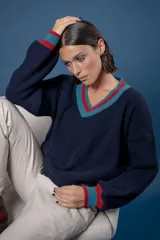 Buzo de punto en color azul marino con escote en V, puños y cuello con detalles en franjas de color turquesa y rojo. Presenta un diseño holgado de manga larga.