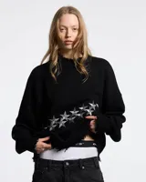 Sweater de punto negro con diseño de estrellas bordadas en color gris en el frente. Presenta cuello, puños y ruedo con terminaciones desflecadas y un corte holgado.