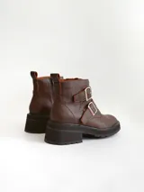 Botas cortas de cuero color marrón con suela track negra. Presentan dos correas ajustables con hebillas metálicas plateadas en el empeine y cierre lateral interno.