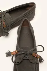 Mocasín estilo náutico de gamuza marrón, con cordones de cuero, borla decorativa y cuentas de colores en el empeine.