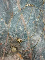 Collar de cadena fina dorada con dos dijes esféricos texturizados e incrustaciones de piedras de colores y zirconias.