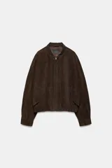 Cazadora tipo bomber de Zara confeccionada en piel de ante 100%. Presenta cuello redondo, cierre frontal con cremallera metálica, bolsillos delanteros con solapa y bajo con acabado elástico.