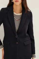 Saco de corte sastrero en color azul marino, con solapas clásicas, cierre frontal de un botón y bolsillos laterales con solapa. Presenta una estructura entallada con hombreras.