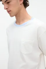 Remera blanca de algodón con textura suave, corte relaxed, manga corta, cuello redondo en contraste de color celeste y un bolsillo aplicado en el pecho.