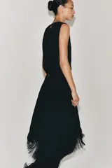 Vestido midi de Zara Woman Collection color negro, sin mangas, con cuello redondo y espalda abierta. Presenta un diseño asimétrico en el bajo adornado con flecos a tono, y cierre trasero con cremallera y botón.