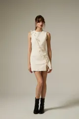 Vestido corto de jean color natural, con corte al cuerpo, cuello a la base y diseño sin mangas. Presenta un detalle de cierre frontal con lazos decorativos y una pequeña abertura lateral.