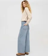 Pantalón de jean corte wide leg con cintura baja y cierre frontal con botón y cremallera. Presenta un diseño de pierna ancha y tiro bajo, confeccionado en algodón resistente con acabado en tono azul claro.
