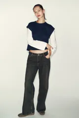 Prenda de manga larga blanca con un chaleco de tejido de punto azul marino superpuesto, creando un efecto de dos piezas. El chaleco es de cuello redondo y corte recto.