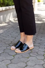 Sandalias bajas negras de cuero charol, con base color suela y diseño minimalista.