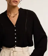 Camisa negra de viscosa sostenible, con escote en V, mangas largas abullonadas con puños elásticos y cierre frontal con botones. Presenta detalles de canalé en los hombros y la espalda.