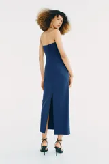 Vestido midi de color azul, con escote recto y cuello halter que incorpora una aplicación metálica tipo choker. Presenta un diseño con frunces laterales en el frente.