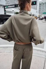 Cazadora estilo bomber color gris, con cuello subido, manga larga, bolsillos delanteros de vivo y cierre frontal con cremallera. Presenta bajo ajustable con cordones elásticos laterales.