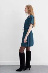 Vestido mini de escote cruzado en color azul petróleo, con mangas cortas y cintura elastizada con lazo ajustable. Presenta detalles de cadenitas metálicas decorativas en los hombros y en la terminación del lazo.