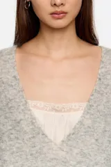 Jersey de punto largo con corte oversize, escote en pico pronunciado y mangas largas con volumen. Incluye un top interior de tirantes en satén con detalles de encaje en el escote.