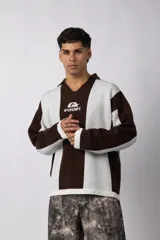 Sweater de tejido de punto con diseño de rayas verticales en tonos beige y blanco. Presenta cuello polo abierto, mangas largas y un corte holgado. Incluye un logo bordado en el centro del pecho.