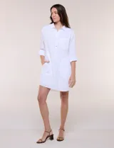 Vestido camisero corto de color blanco con sutiles rayas verticales, de la marca Dash. Presenta cuello con solapa, escote en V con botones parciales en el frente, bolsillo superior en el pecho y bolsillos laterales de gran tamaño. Cuenta con mangas largas de largo regulable mediante presilla y botón, calce holgado y ruedo trasero más largo.