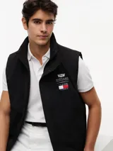 Chaleco negro con cuello chimenea, cierre de cremallera oculto con botones a presión y dos bolsillos laterales ribeteados. Presenta logos bordados en el pecho de Tommy Hilfiger y Cadillac Formula 1 Team.