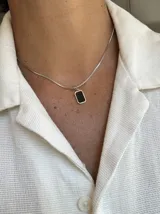 Collar con cadena de eslabones tipo caja plateada y un dije rectangular con borde plateado y centro de piedra negra pulida.