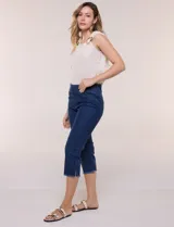 Capri blanco de corte ajustado, con tiro alto y pretina ancha elastizada tipo faja. Presenta bolsillos falsos al frente con remaches, piernas entalladas con pequeñas aberturas en los laterales y ruedo desflecado.
