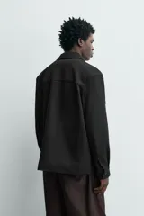 Sobrecamisa relaxed fit color beige con tejido elástico, cuello solapa, manga larga con puños abotonados, bolsillos de plastrón con solapa en el pecho, bolsillos laterales de vivo en la cadera y cierre frontal de botones.