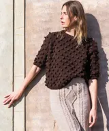 Sweater marrón de manga corta confeccionado en 100% lana merino con textura de bodoques tridimensionales en relieve y cuello redondo a la base.