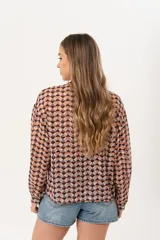 Camisa de gasa traslúcida con estampado geométrico de rombos en tonos naranja, violeta y negro. Presenta cuello camisero, cierre frontal con botones y un detalle de volado a lo largo de la cartera. Posee mangas largas con puños abotonados y un calce fluido.