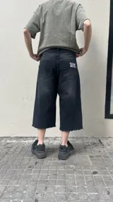 Bermuda de jean negra con lavado oscuro, corte ancho (baggy) y largo hasta la rodilla (3/4). Presenta un dobladillo deshilachado en el ruedo y cierre frontal con botón y cremallera.