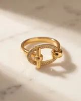 Anillo de acero quirúrgico dorado con diseño ovalado y aplique transversal, decorado con circones en su estructura.