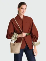 Bolso tipo cubo Longchamp modelo Le Roseau XS, color beige claro, con cierre metálico dorado en forma de barra. Incluye correa larga ajustable para llevar cruzado.